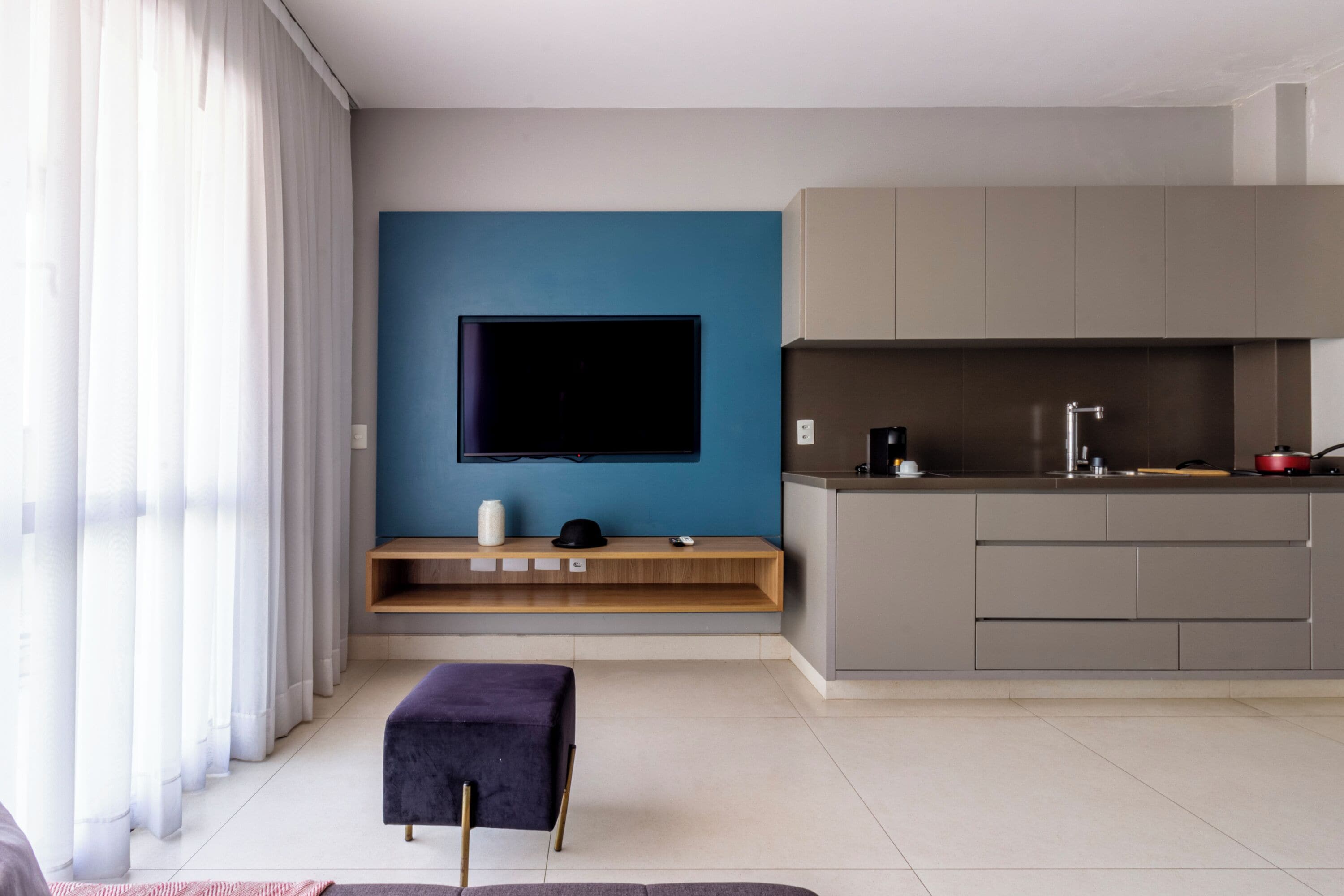 A modern living room with a flat-screen TV, a wooden console table, and a kitchen area with grey cabinets.