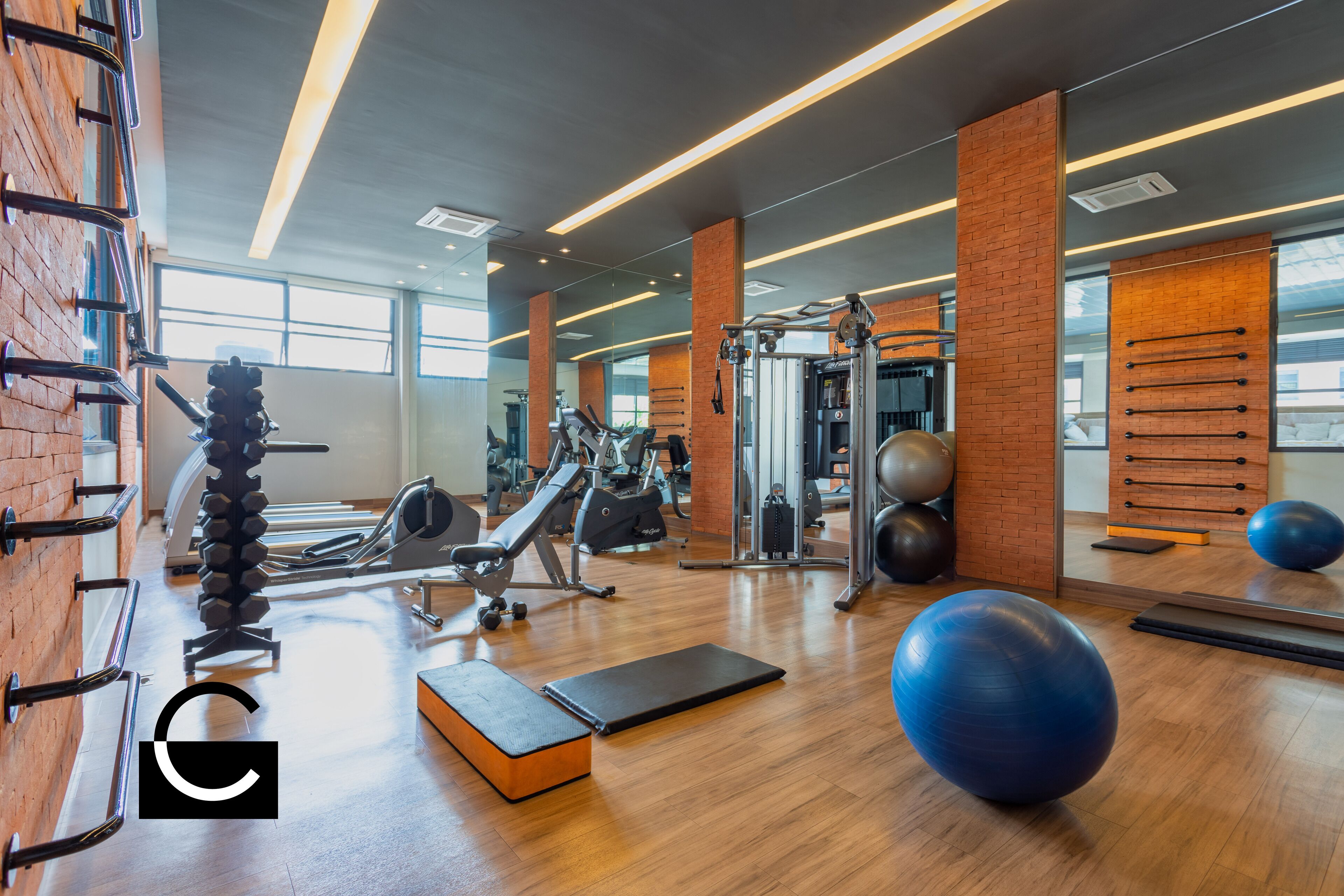 A gym with exercise equipment, wooden flooring, and large windows.