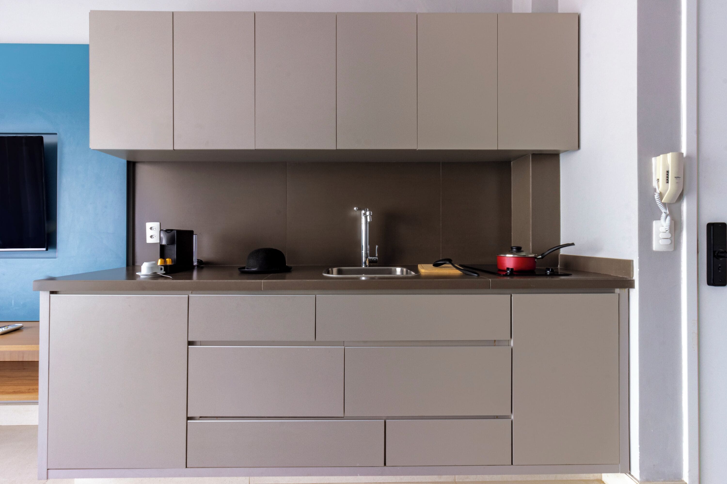 A modern kitchen with grey cabinets, a sink, a red pot, and a telephone.