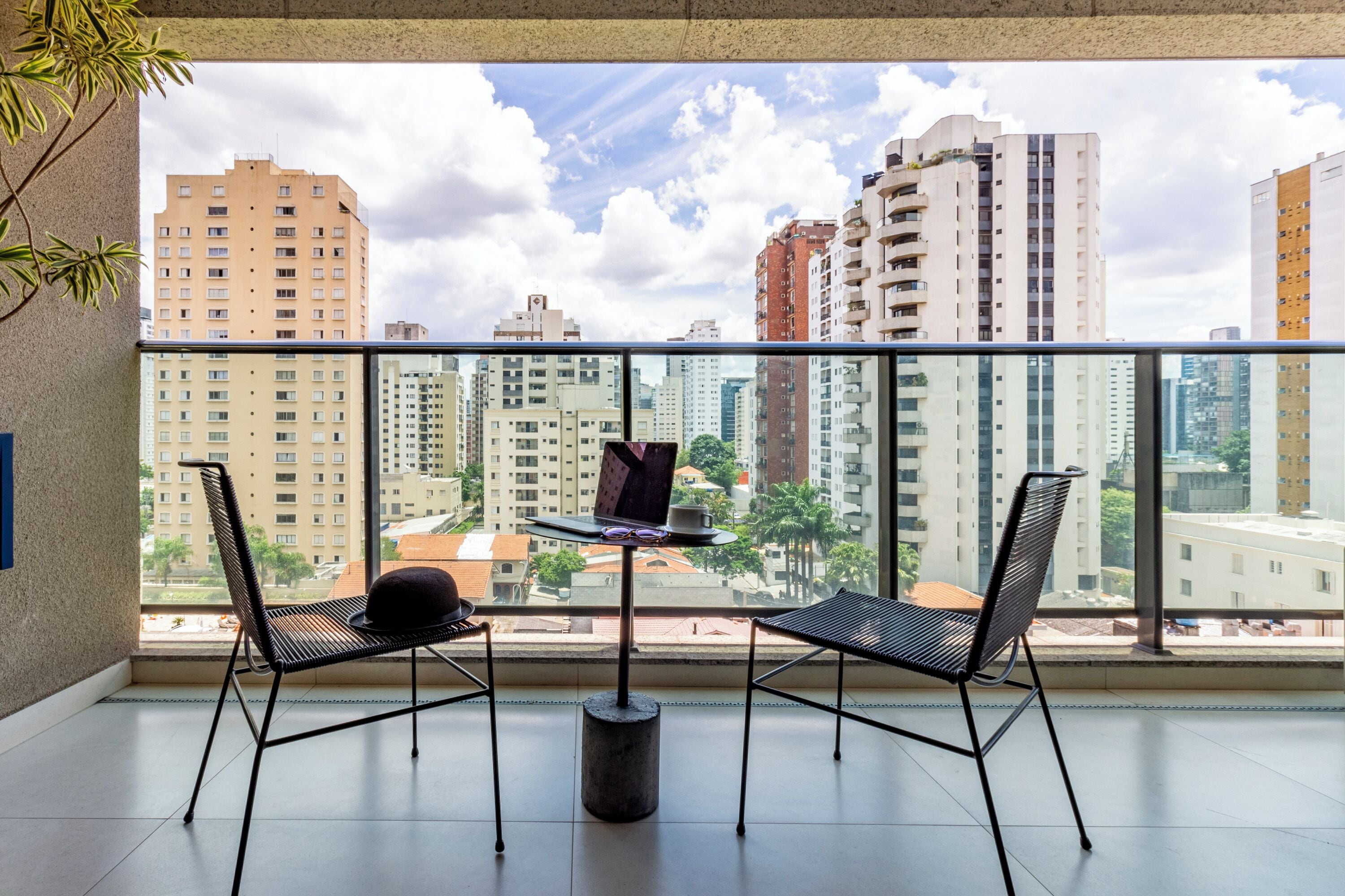 A balcony with two chairs, a small table, and a view of a cityscape with tall buildings.