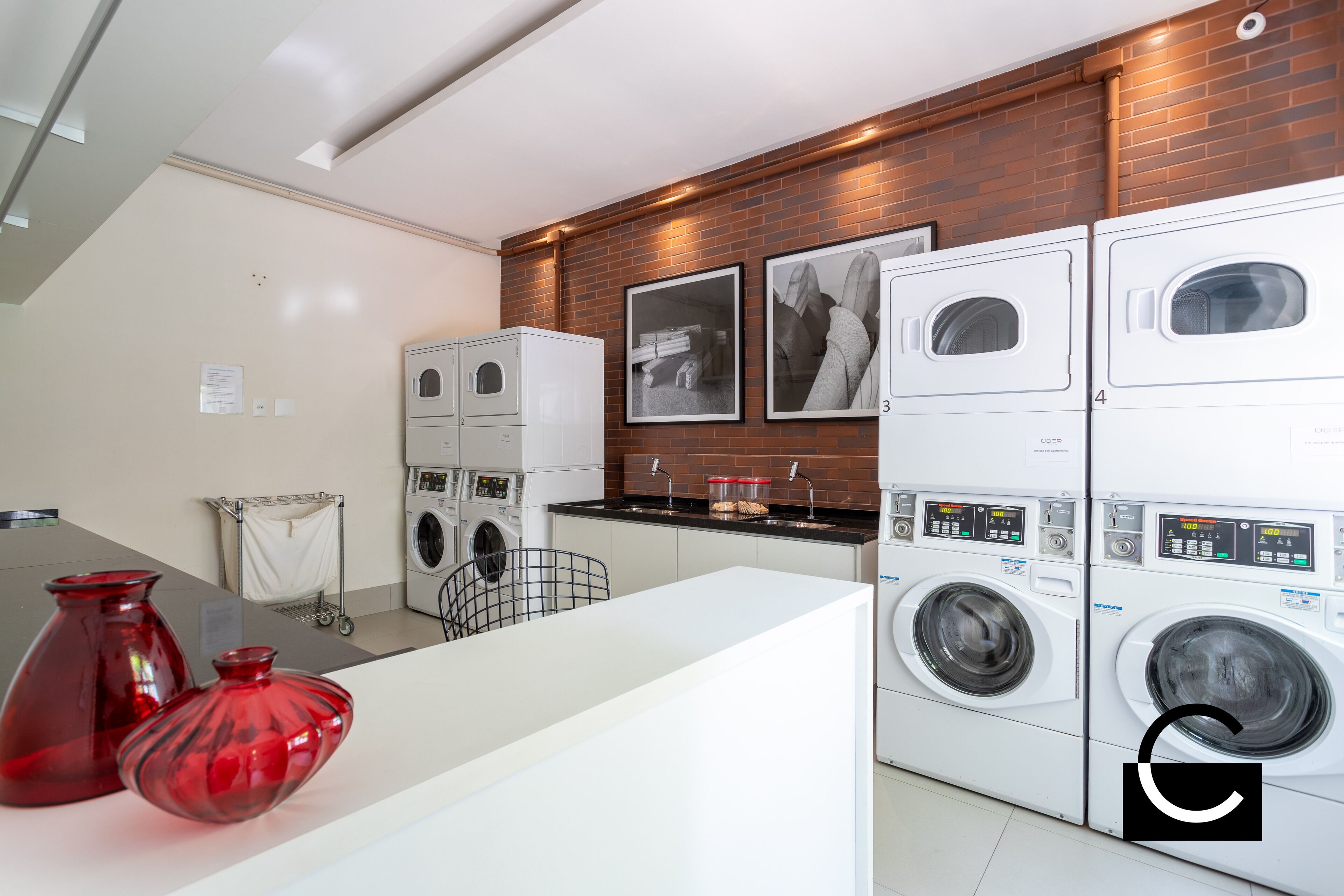 A modern laundry room with stacked washing machines, a metal rack, and two red vases on a counter.