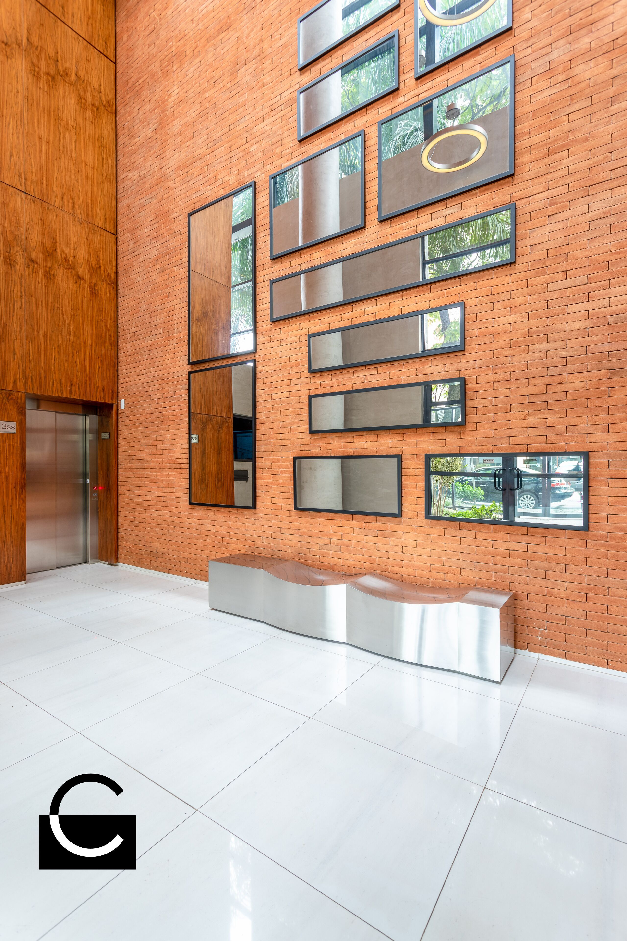 A lobby with a brick wall, large mirrors, and a modern elevator.