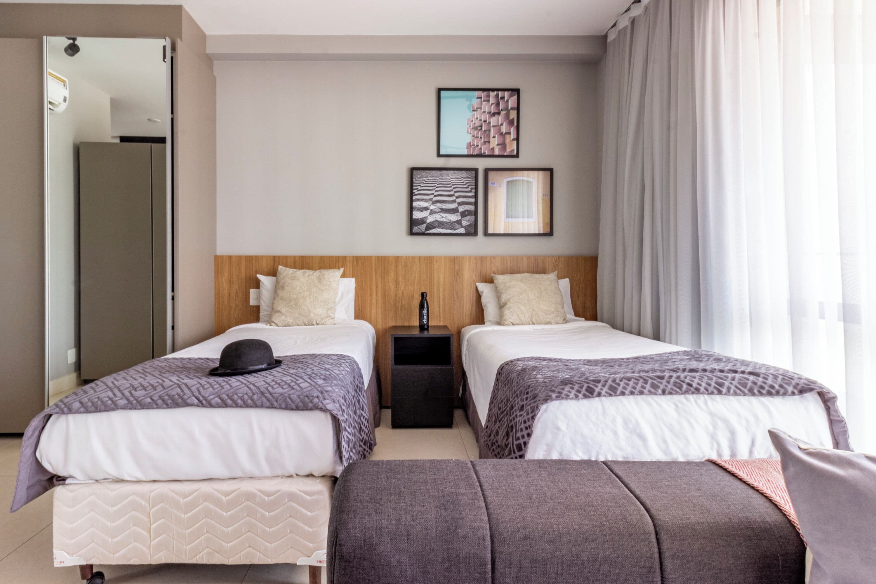 A hotel room with two beds, a wooden headboard, a nightstand, and a view of the cityscape through the window.