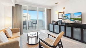 A modern hotel room with a balcony, a dining area, and a TV displaying a pool view.