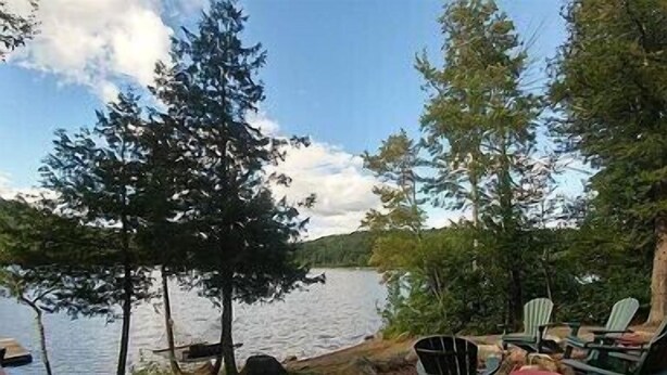 Un espace aménagé au bord du lac, avec des chaises Adirondack et une petite table, entouré d’arbres et d’un quai.