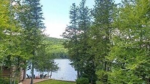Un chalet au bord du lac, doté d’une terrasse offrant une vue sur l’eau, et entouré d’une forêt dense.