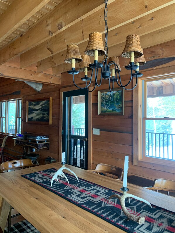 A wooden interior with a chandelier, wooden walls, a table with a patterned runner, and artwork.