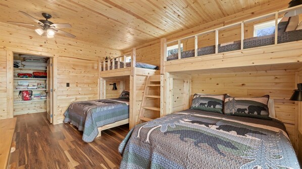 A cozy cabin with two bunk beds, a loft bed, wooden walls, a ceiling fan, and a small window.