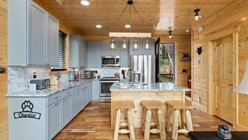 A modern kitchen with grey cabinets, a central island, wooden stools, and a dog paw decal.