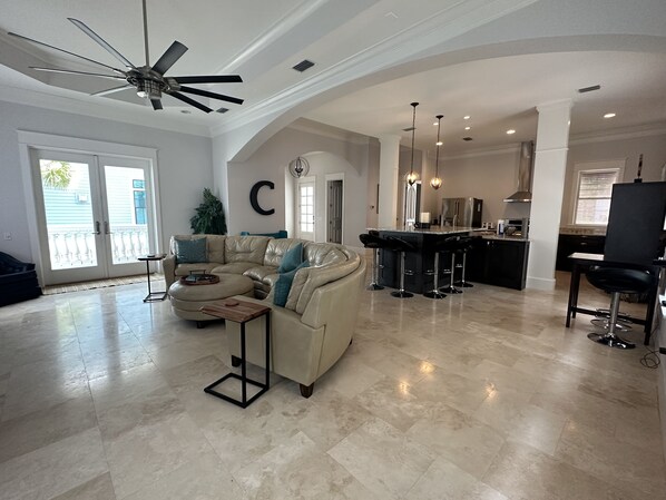 A spacious living room with a large L-shaped sectional sofa, a ceiling fan, and a kitchen area with a bar stool set.