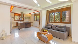 A modern living room with a sofa, a curved coffee table, and a kitchen area with a central island. - Prestige Residence Rhodes - accommodating up to 22 guests! (Ialisos)