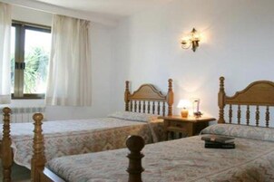 Habitación de hotel con dos camas, una mesita de noche, una lámpara y una ventana con cortinas.