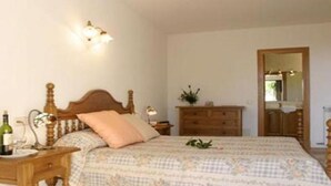 A bedroom with a wooden bed, a nightstand with a bottle, a dresser, and a mirror. - Villa Llobets I (Llucmajor)