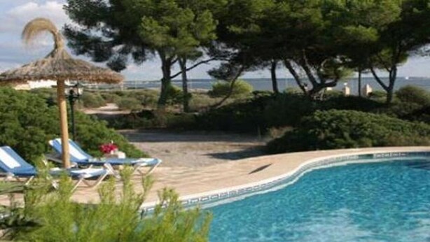 A swimming pool with lounge chairs and a thatched umbrella, surrounded by trees and a view of the sea. - Villa Llobets I (Llucmajor)