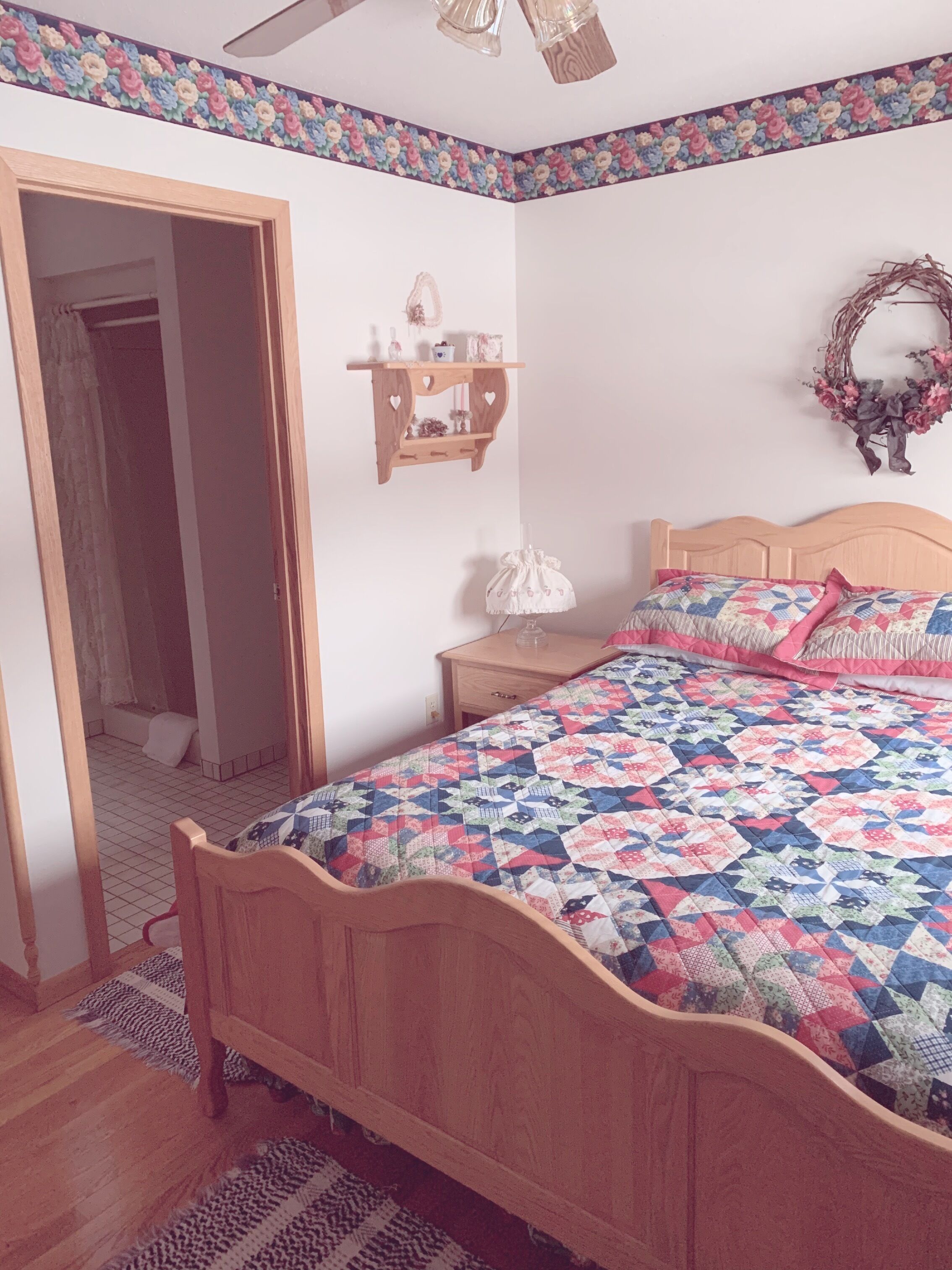A bedroom with a wooden bed, a nightstand, a dresser, a mirror, and a floral-patterned border on the walls.