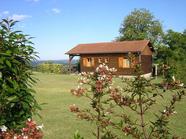 A wooden cabin with a red roof, surrounded by a well-maintained lawn and flowering plants. - Sunset. Unspoiled nature, beautiful views, private pool, pond in the Périgord Noir (Badefols-d'Ans)