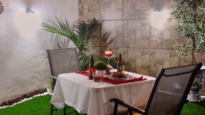 Un espace de restauration en plein air agrémenté d’un mur en pierre, d’une table recouverte d’une nappe blanche, de chaises et de guirlandes lumineuses.