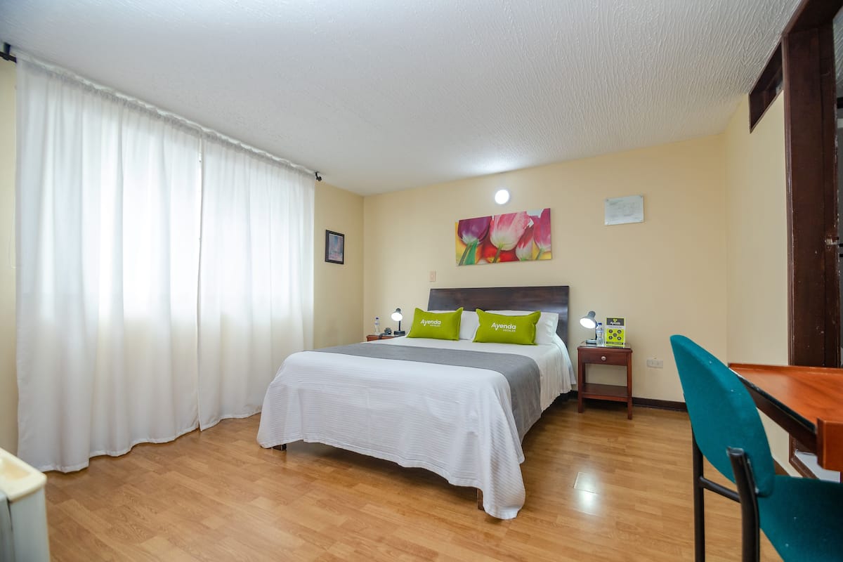 Ein Hotelzimmer mit einem Bett, einem Schreibtisch, einem Stuhl, einem Nachttisch und einem Bild an der Wand.