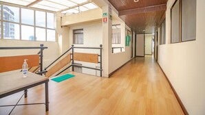 A hallway with wooden flooring, a bench, a table with a bottle, and a green mat.