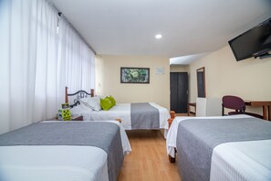 A hotel room with two single beds, a desk, a chair, a television, and a door leading to another room.