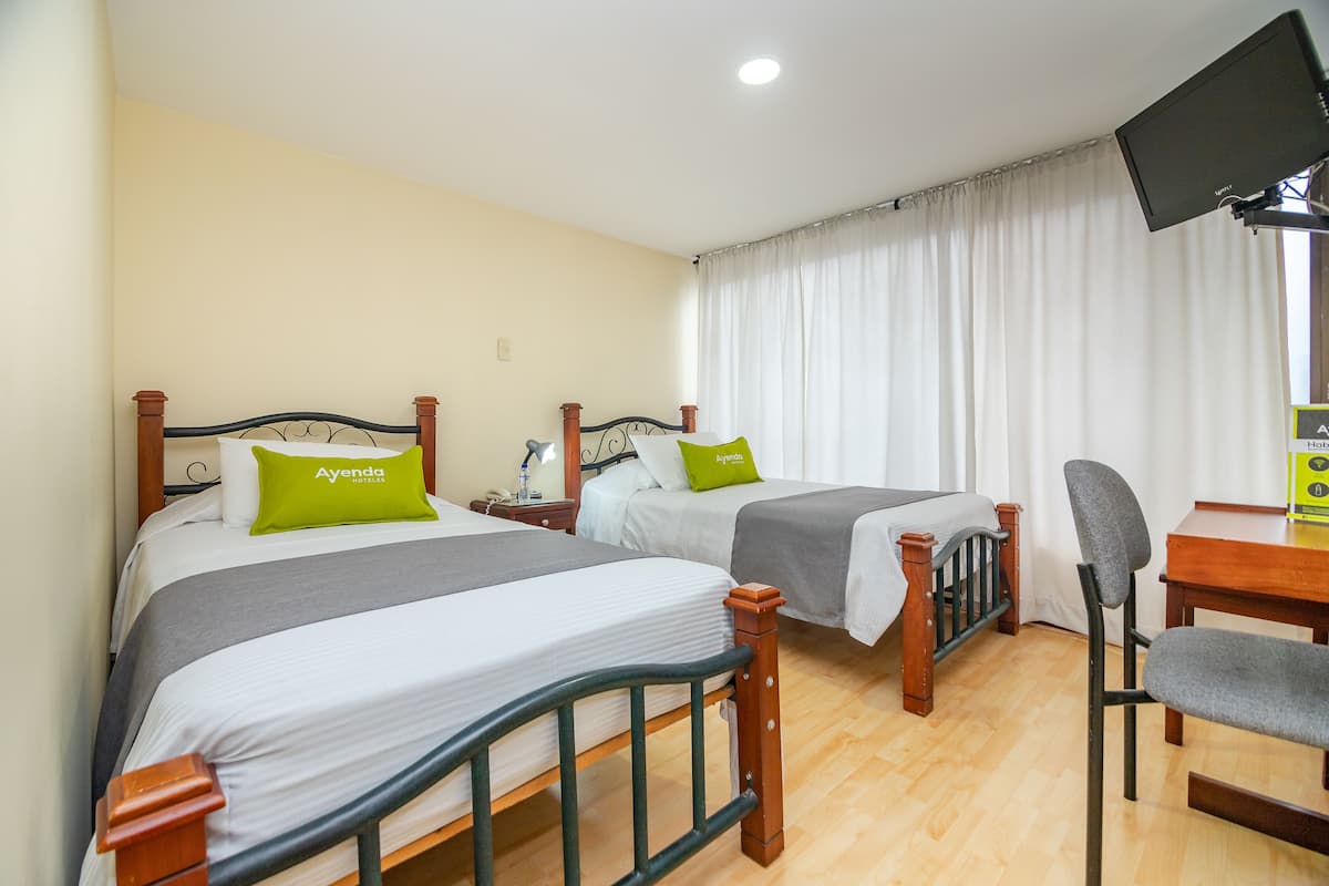 Ein Hotelzimmer mit zwei Betten, einem Schreibtisch, einem Sessel und einem Fernseher.