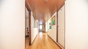 A long, narrow hallway with wooden floors and walls, leading to a bright room at the end.