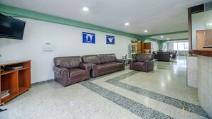 A spacious lobby with a large brown leather sofa, a wooden bookshelf, and a television mounted on the wall.