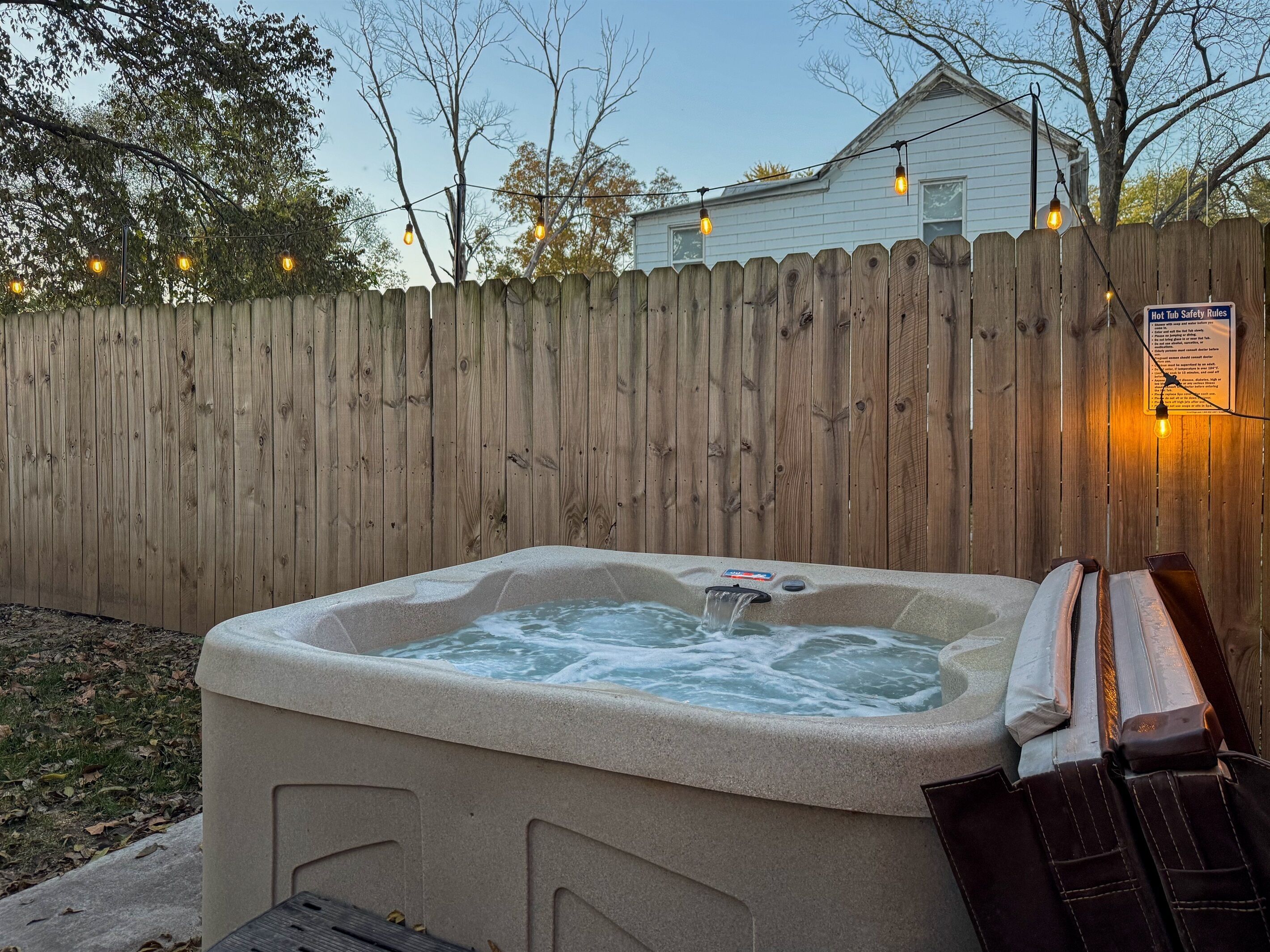 A hot tub with a wooden fence and string lights in the background.