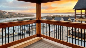 Un balcon en bois offrant une vue sur une rivière et des bâtiments éloignés, au coucher du soleil.