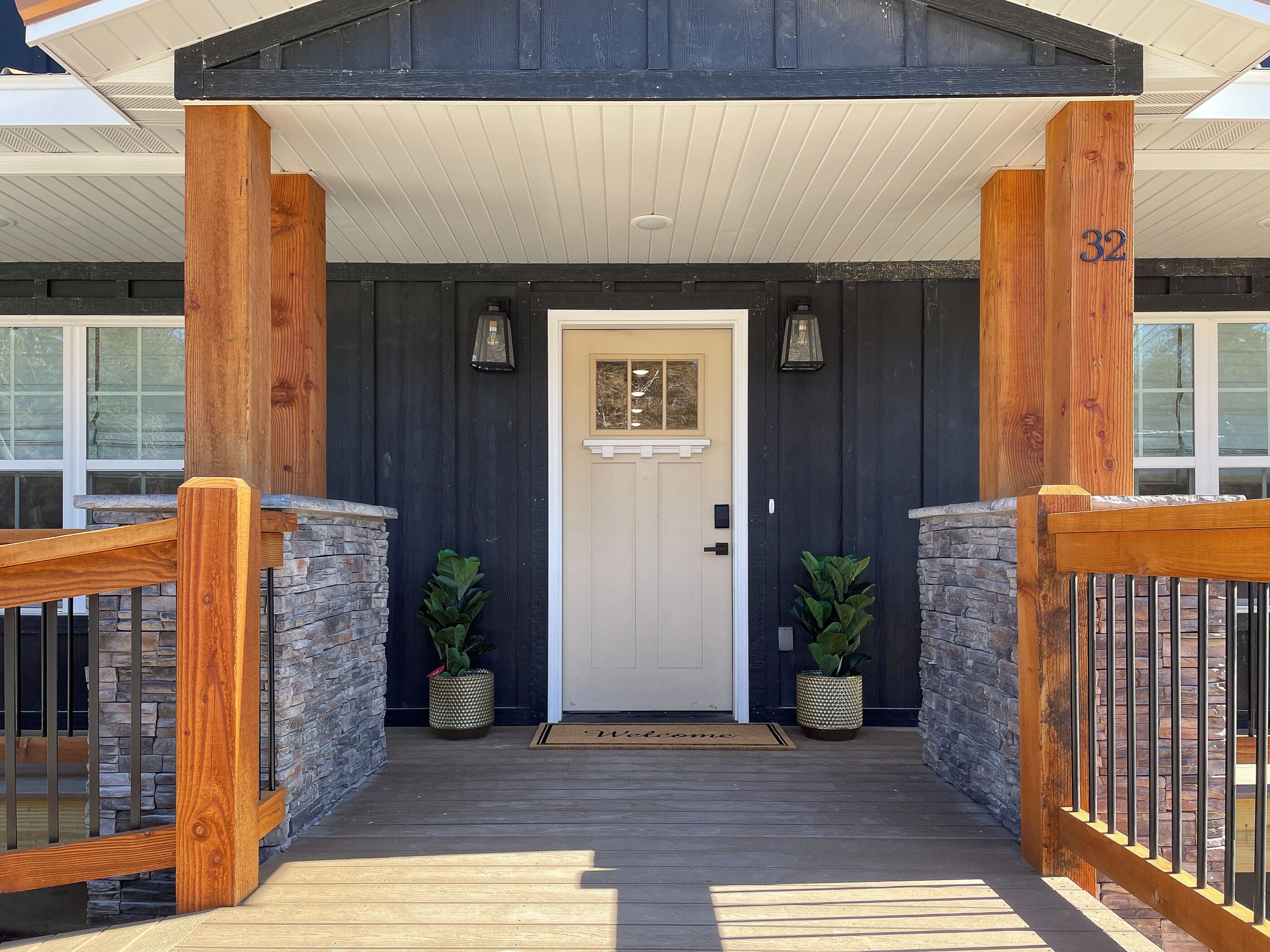 A wooden front porch with a white door, two potted plants, and a welcome mat.