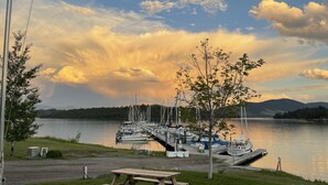 A lakeside marina with boats docked, a picnic table, and a grassy area.