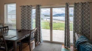 A room with a dining table, chairs, and a view of a lake and mountains through large windows and curtains.