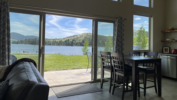 A spacious living area with a sliding glass door leading to a patio with a view of a lake and mountains.