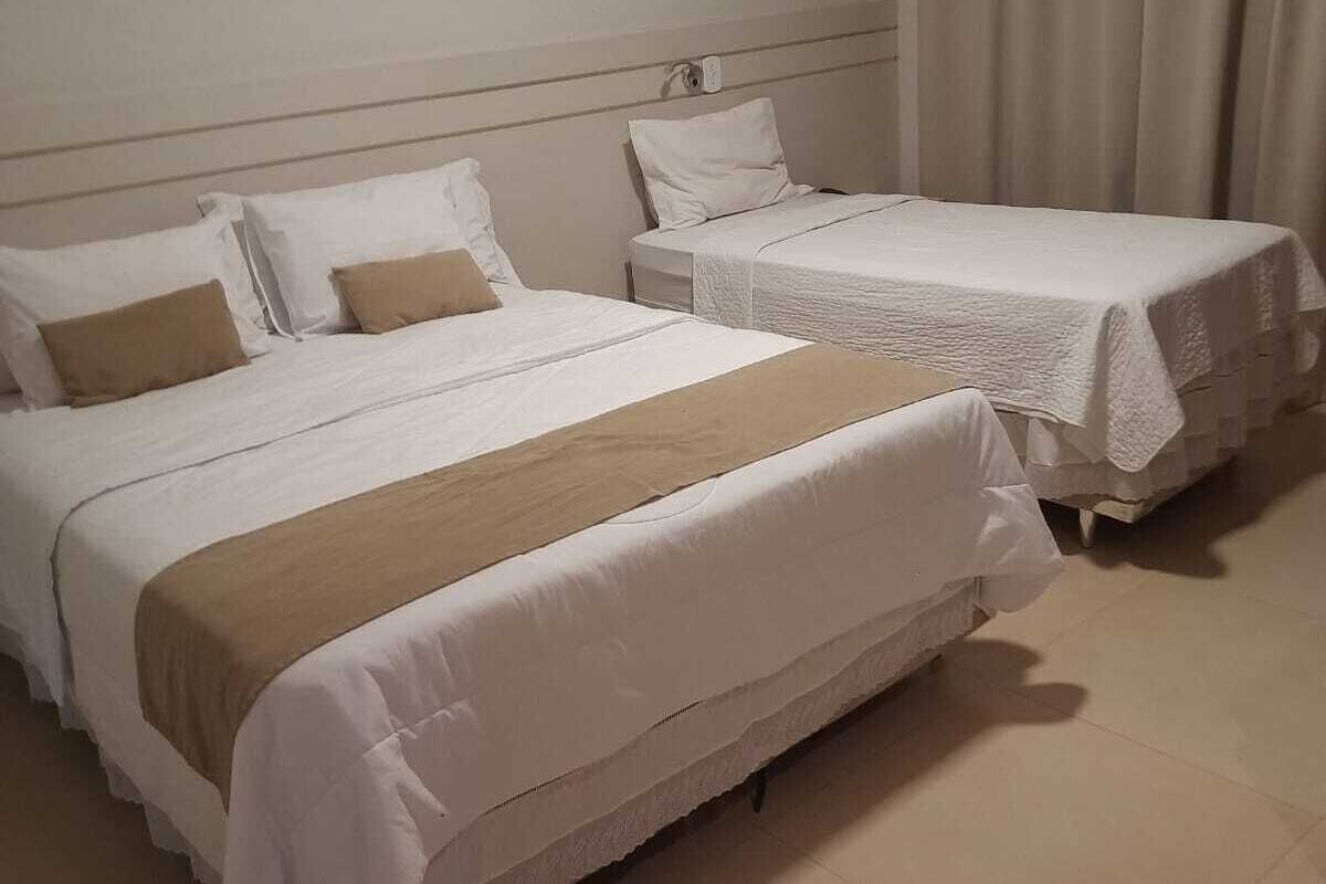 Een hotelkamer met twee eenpersoonsbedden, elk met witte lakens en een bruine plaid.