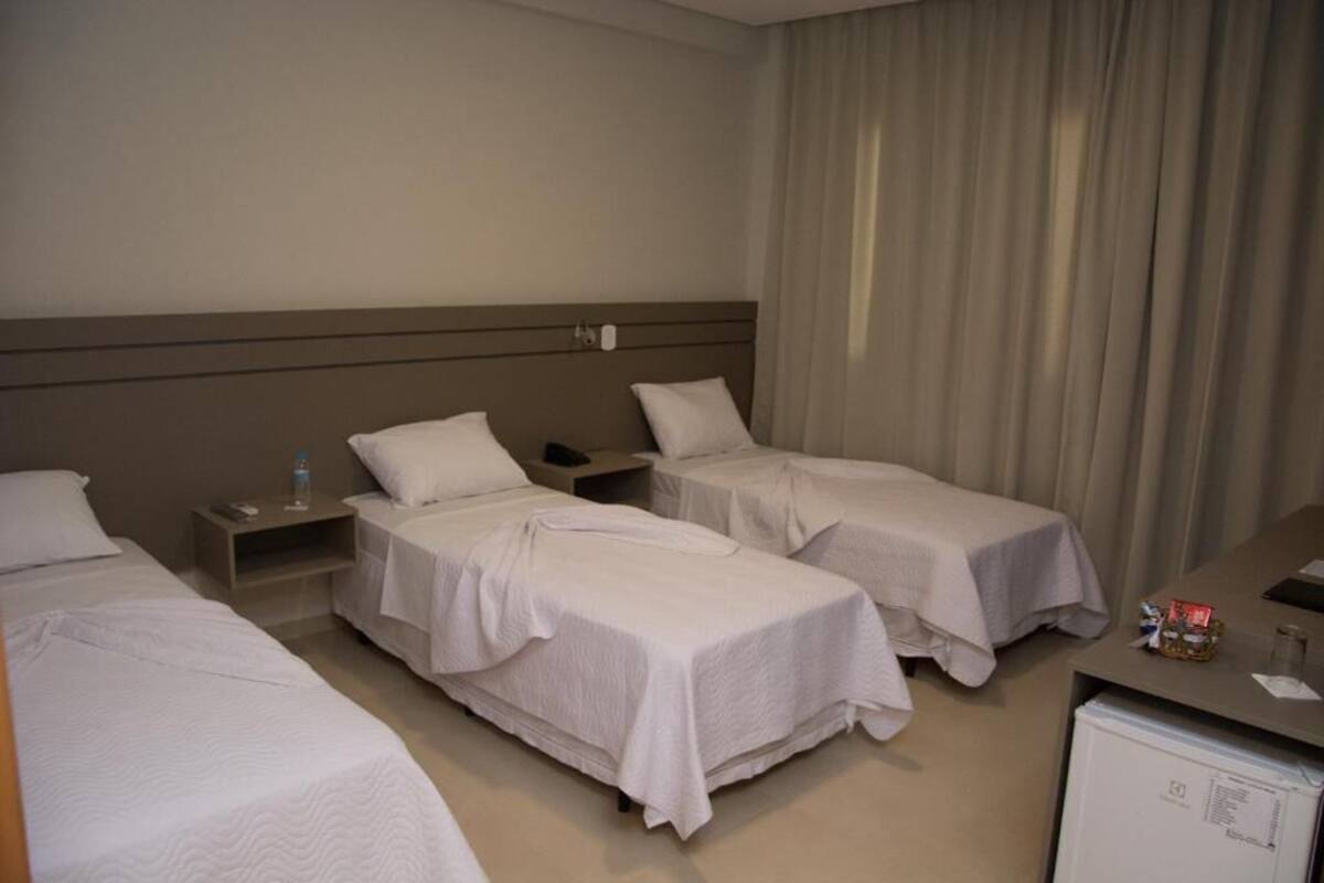 Een hotelkamer met twee eenpersoonsbedden, een bureau, een stoel, een kleine koelkast en een raam met gordijnen.