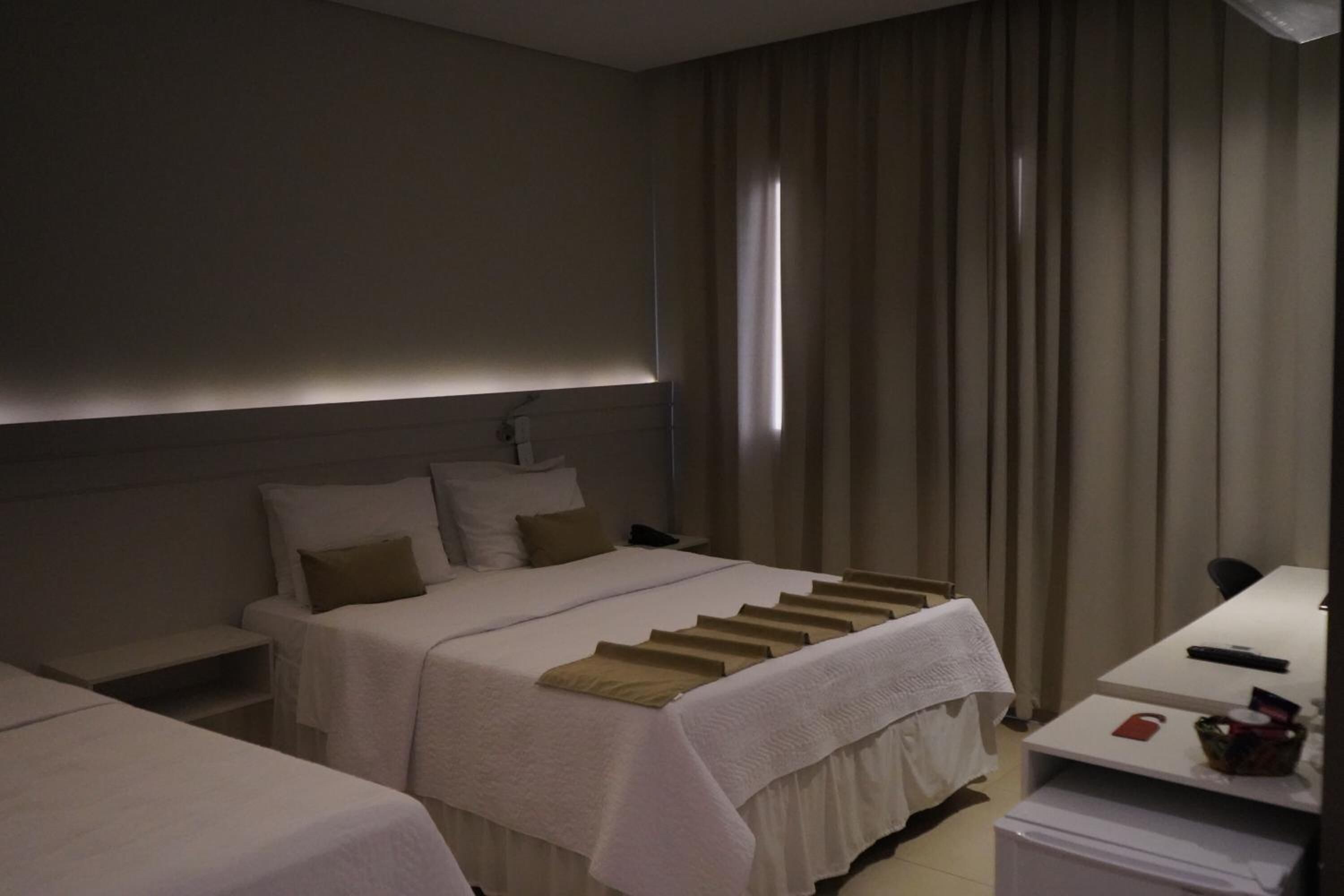 A hotel room with two beds, a desk, and a window with curtains.