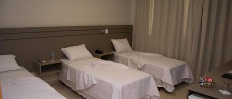 A hotel room with two single beds, a desk, a chair, and a small refrigerator.