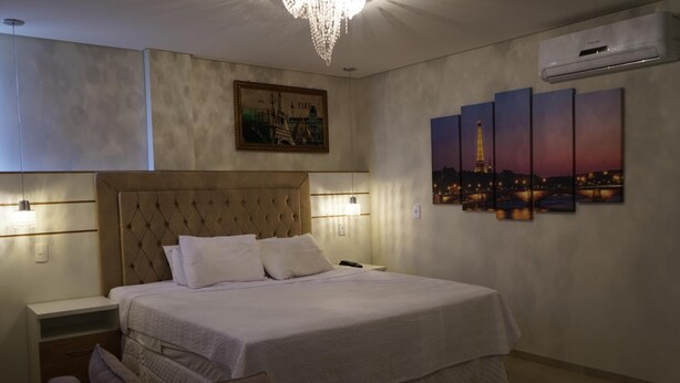 Un dormitorio con una cama grande, mesitas de noche, un candelabro, obras de arte en la pared y un equipo de aire acondicionado.