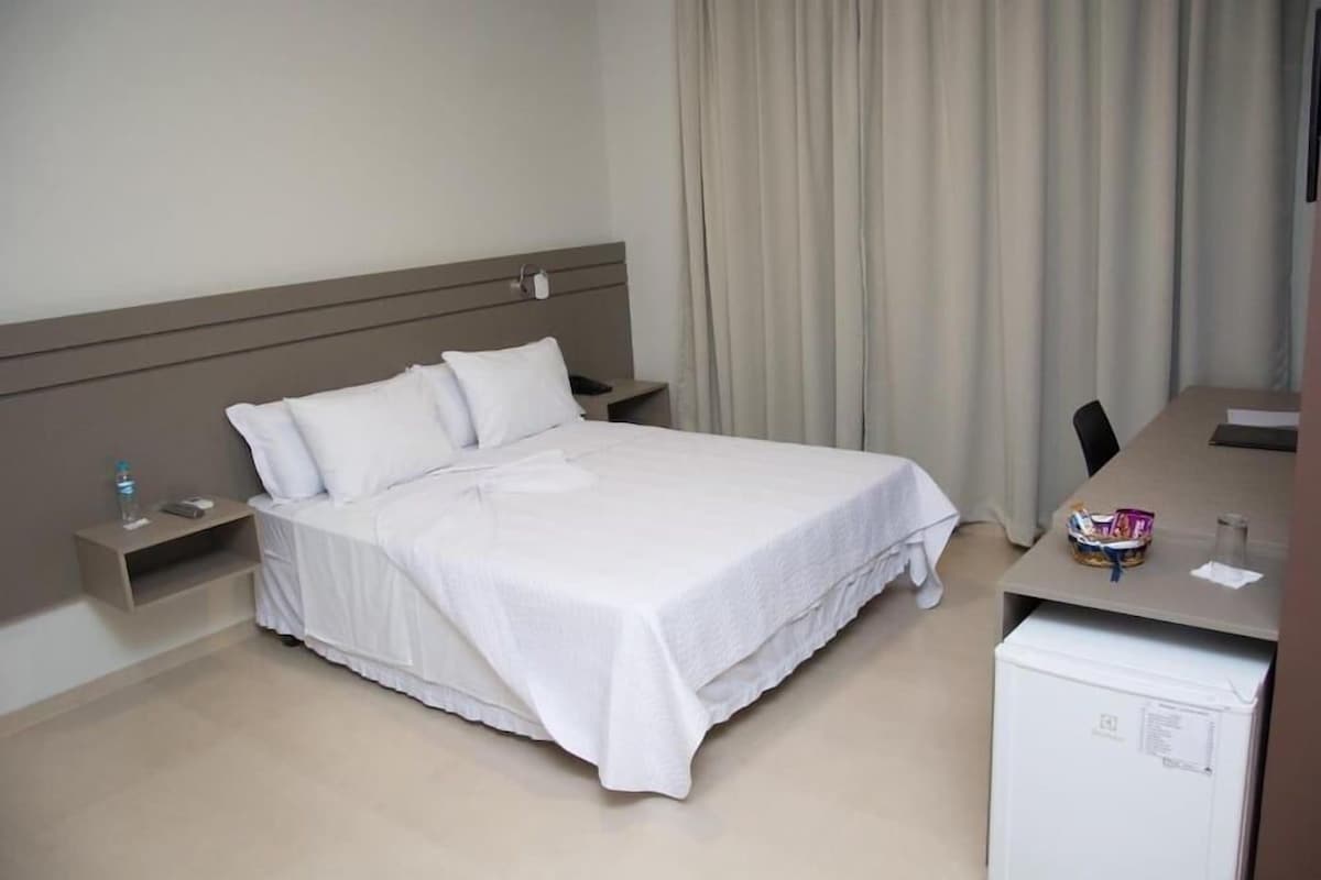 Een hotelkamer met een bed, een bureau, een stoel, een nachtkastje en een minibar.