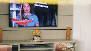 Una sala de estar con una televisión de pantalla plana montada en la pared, una mesa de centro con libros y un florero, y un sofá.