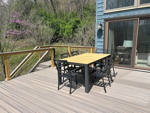 Une terrasse en bois avec une table et des chaises, une porte vitrée et une rambarde.
