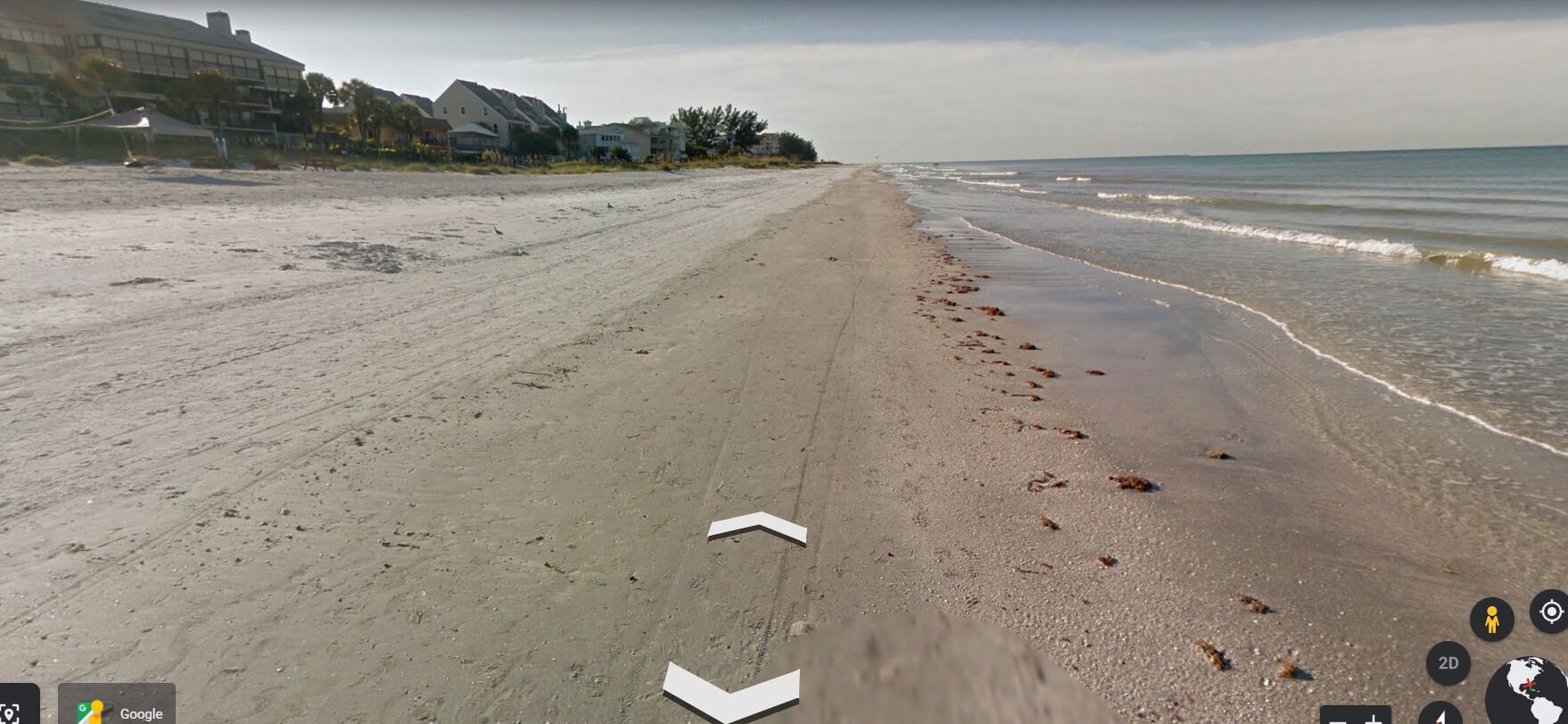 A beach with a clear path leading to the water, a few footprints, and buildings in the background.