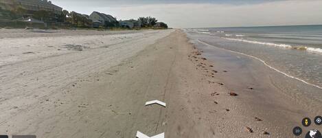 A beach with a clear path leading to the water, a few footprints, and buildings in the background.