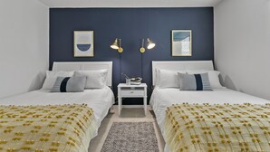 A bedroom with two beds, a nightstand, and wall-mounted lamps.