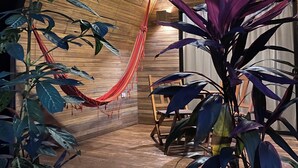 Une pièce aux murs en bois, avec un hamac et diverses plantes.