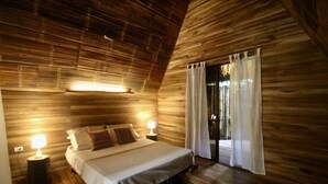 A bedroom with a wooden sloped ceiling, a bed with pillows, two bedside lamps, and a sliding glass door to the outside. - Buena Onda - Bungalow Zuma few steps to the beach (Playa Hermosa)