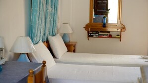 A bedroom with two beds, a bedside table with a lamp, a mirror, and a shelf with books and a vase. - Amphitrite Apartments (Kalymnos)