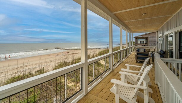 Eine Holzterrasse mit weißen Geländern, die auf einen Strand blickt.