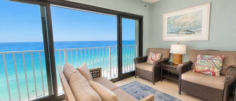 A balcony with a view of the ocean, a ceiling fan, wicker furniture, and a rug.
