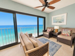 A balcony with a view of the ocean, a ceiling fan, wicker furniture, and a rug.